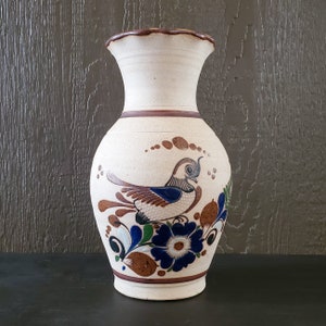 May include: A white ceramic vase with a brown rim and a painted design of a blue and brown bird with brown and green floral accents.