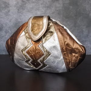 May include: A silver and brown leather handbag with a unique geometric design. The bag has a flap closure and a quilted texture.