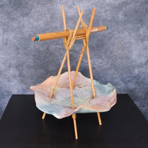 Peut inclure: Sculpture décorative artisanale avec un bol en céramique aux couleurs pastel, soutenu par des pieds en bambou. Des tiges de bambou sont attachées au-dessus du bol, avec une petite section peinte en bleu et orange.