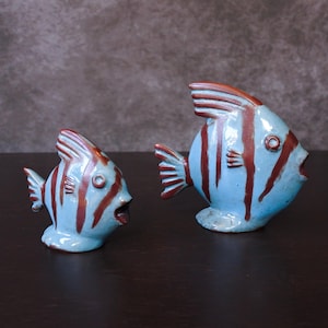 Może przedstawiać: Dwie ceramiczne figurki ryb w niebiesko-brązowe paski. Większa ryba jest po prawej, a mniejsza po lewej.