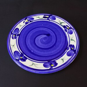 Könnte beinhalten: Ein blauer Keramikteller mit weißem Rand und einem Wirbelmuster in der Mitte. Der Rand ist mit einem floralen Muster aus violetten Blüten mit gelben Zentren verziert.