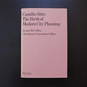 May include: A hardcover book titled "Camillo Sitte: The Birth of Modern City Planning" by George R. Collins and Christiane Crasemann Collins. The book has a light pink cover with black text and the Rizzoli logo.