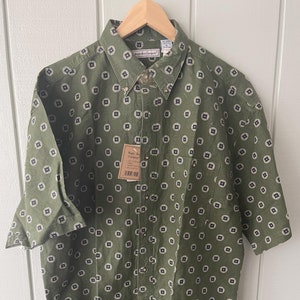 May include: A green short-sleeved button-down shirt with a white and black geometric pattern. The shirt has a pocket on the left chest and a brand tag that reads "Eagle Boy Company".