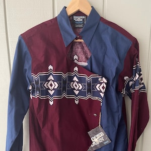 May include: A maroon and blue long-sleeved shirt with a geometric pattern. The shirt has a split collar and a tag that reads "Brooks & Dunn" and "Guys & Dolls".