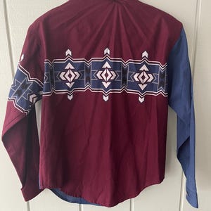 May include: A long-sleeved button-down shirt with a maroon body and blue sleeves. The shirt has a geometric pattern in white, blue, and black across the chest.