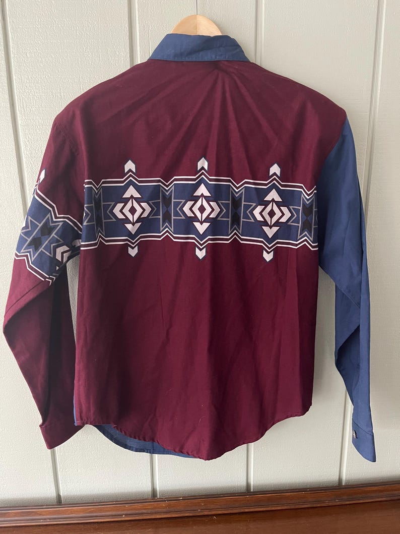 May include: A long-sleeved button-down shirt with a maroon body and blue sleeves. The shirt has a geometric pattern in white, blue, and black across the chest.