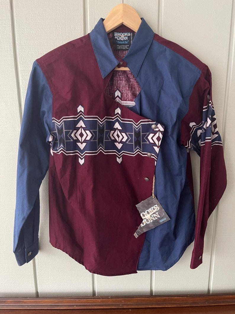 May include: A maroon and blue long-sleeved shirt with a geometric pattern. The shirt has a split collar and a tag that reads "Brooks & Dunn" and "Guys & Dolls".