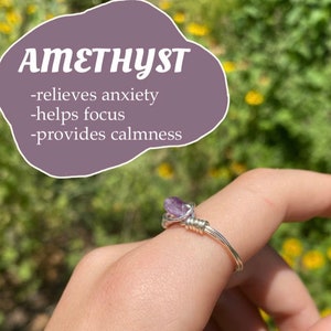 May include: Amethyst ring with a silver wire wrap. The ring features a purple amethyst stone. The text "Amethyst" is written in white on a purple background. The text below reads "relieves anxiety", "helps focus", and "provides calmness".