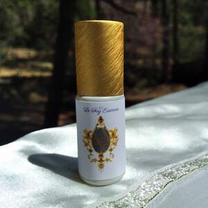 Puede incluir: Un frasco de rodillo dorado y blanco con una etiqueta que dice "Le Fay Essences" y "Divine Dragon".