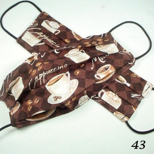 May include: Two brown fabric face masks with elastic ear loops. The masks feature a repeating pattern of coffee cups and coffee beans with the word "Cappuccino" printed on the fabric.
