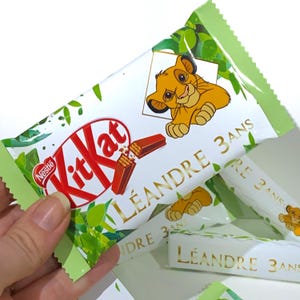 May include: A green and white Kit Kat chocolate bar wrapper with a cartoon lion cub and the text "LÉANDRE 3 ANS".