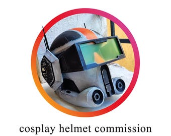 May include: A detailed cosplay helmet with a black, gray, and orange color scheme. The helmet features a visor with green and orange tints, and two small antennas. The text "cosplay helmet commission" is displayed below the helmet.