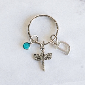 May include: Silver keychain with a dragonfly charm, a turquoise blue gemstone, and a silver letter D charm.