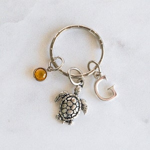 May include: Silver key chain with a silver turtle charm, a silver letter G charm, and a small amber-colored bead.