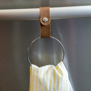 May include: A brown leather strap with a metal ring attached to a stainless steel bar. A yellow and white striped kitchen towel is hanging on the ring.