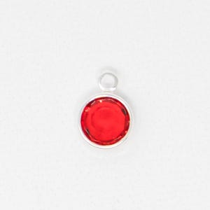 May include: A round, red gemstone pendant with a silver-colored bezel and a small loop at the top. The pendant is set against a white background. The gemstone is a vibrant, solid red color.