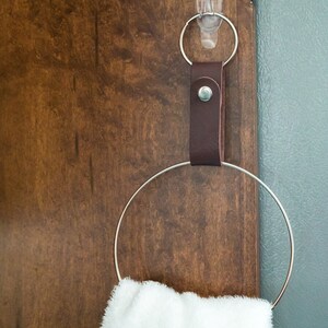 May include: A brown leather strap with a metal ring attached to a silver hook. The ring is holding a white towel.