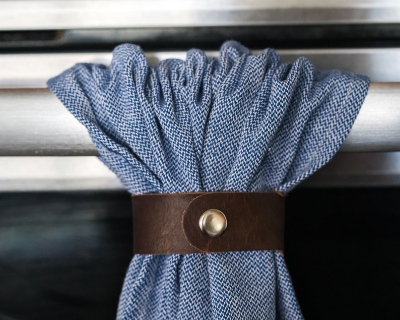 May include: A blue and white patterned fabric kitchen towel with a brown leather strap and a metal buckle. The towel is hanging on a silver oven door.