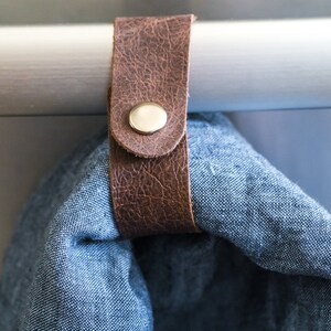 May include: A brown leather strap with a metal button is attached to a white bar. A blue fabric is hanging from the strap.