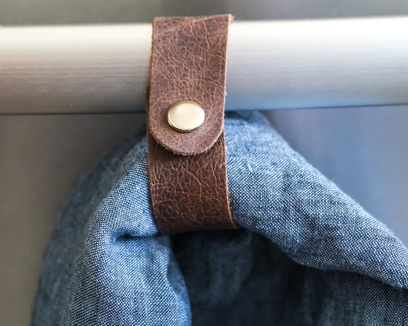 May include: A brown leather strap with a metal button is attached to a white bar. A blue fabric is hanging from the strap.