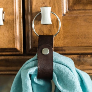 May include: A brown leather towel ring with a silver ring attached to a cabinet door. A light blue towel is hanging on the ring.