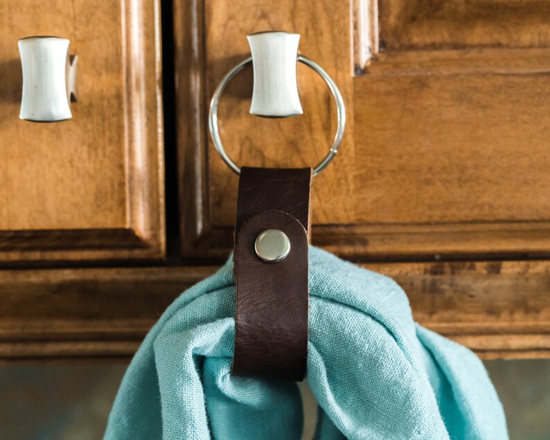 May include: A brown leather towel ring with a silver ring attached to a cabinet door. A light blue towel is hanging on the ring.