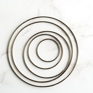 May include: Four silver metal hoops of different sizes, nested inside each other, on a white marble background.