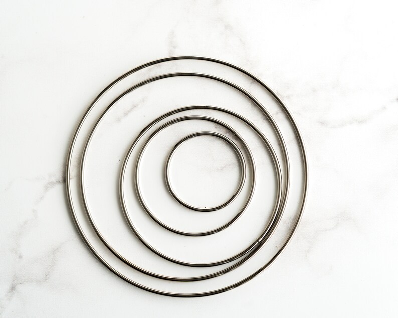 May include: Four silver metal hoops of different sizes, nested inside each other, on a white marble background.