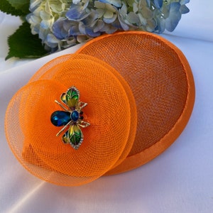 May include: Orange and green bee-shaped hat pin with a blue jewel on a bright orange mesh hat.