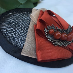 May include: A black and brown hat with a red ribbon and a silver brooch with red beads.