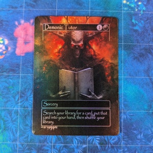 May include: A Magic: The Gathering card with a black background and a red and orange illustration of a demon holding a book. The card text reads "Demonic Tutor" and "Search your library for a card, put that card into your hand, then shuffle your library."