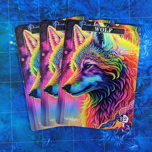 May include: Three colorful playing cards with a rainbow wolf illustration. The card reads "WOLF" in black text. The cards are on a blue background.