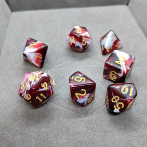 May include: Set of six red and white swirl dice with gold numbers. The dice are in a gray box.