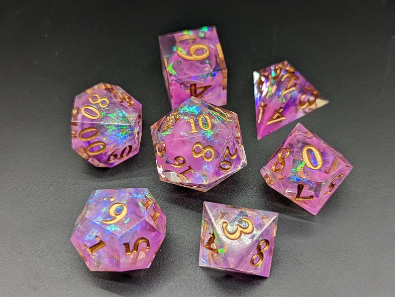 May include: Set of seven iridescent purple dice with gold numbers. The dice are a d4, d6, d8, d10, d%, d12, and d20.