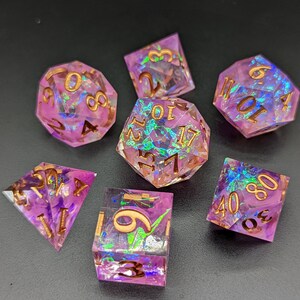 May include: Set of seven iridescent purple and gold dice with a variety of shapes and numbers. The dice have a glittery, holographic finish.