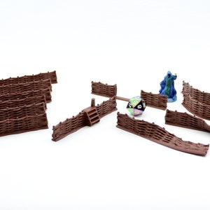 Peut inclure: Un ensemble de clôtures miniatures en plastique brun pour jeux de table. L'ensemble comprend des sections droites et courbes, ainsi qu'une petite porte avec des marches. Une figurine miniature et un dé sont également visibles sur l'image.