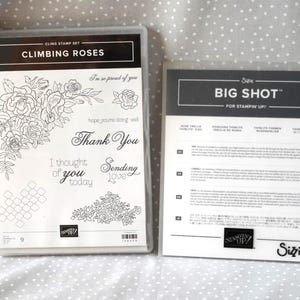May include: Two clear plastic stamp sets. One set is labelled "Climbing Roses" with floral designs and sentiments such as "Thank You." The other set is labelled "Big Shot" and includes instructions. Both sets are on a white dotted background.