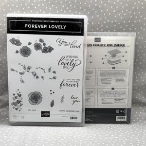 May include: A clear plastic package containing a photopolymer stamp set labelled "FOREVER LOVELY" with floral and heart designs, and phrases like "You are loved" and "Happy Valentine's Day". Next to it is a package of "ERS EDGELITS DIES".