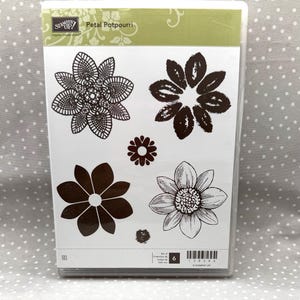May include: A clear plastic case containing a Stampin' Up! Petal Potpourri rubber stamp set. The insert displays six dark brown floral and leaf designs on a white background, including a detailed mandala-style flower and a textured daisy.