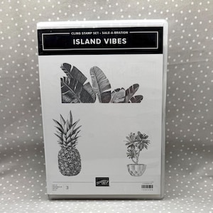 May include: A rectangular white plastic case containing a cling stamp set titled Island Vibes. The cover features black line art illustrations of tropical banana leaves, a pineapple, and a small potted plant, with the Stampin' Up logo at the bottom.