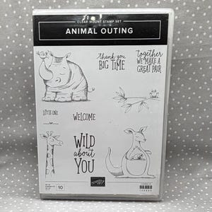 May include: A clear plastic case containing a clear-mount stamp set titled ANIMAL OUTING. The set features black line art illustrations of a rhinoceros, a giraffe, a kangaroo with a joey, and a frog on a branch, alongside text phrases.