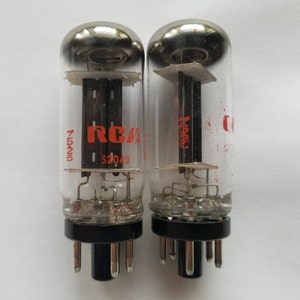 May include: Two vintage vacuum tubes with clear glass bulbs and black bases. The tubes have internal components and the text "RCA" in red. One tube has the number "52049" printed on it.