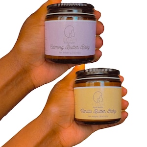 May include: Two glass jars of Edah body butter with black screw-on lids. The top jar has a light purple label reading Calming Butter Baby, and the bottom jar has a yellow label reading Vanilla Butter Baby. Both labels state Net Weight 2.2 oz | 62 g.