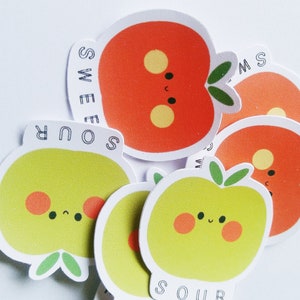 May include: A set of six colorful stickers featuring cartoon apples with happy faces. The stickers have the words "Sour" and "Sweet" written on them.