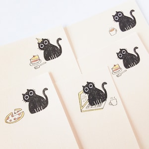 May include: Four black cat illustrations on white note cards. Each card features a different cat with a different activity, including eating cake, drinking coffee, eating pizza, and working on a laptop.
