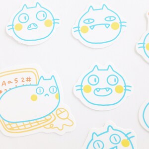 May include: A set of six stickers featuring cartoon cats with different expressions. The cats are outlined in blue and have yellow cheeks. The stickers are on a white background.
