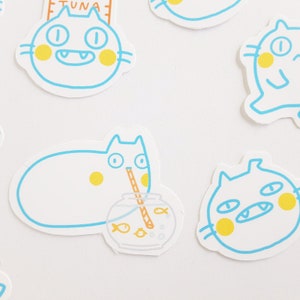 May include: A set of five stickers featuring cartoon cats with different expressions. The cats are outlined in blue and have yellow accents. One cat is drinking from a fishbowl with a straw.