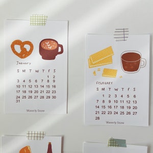 May include: A calendar with illustrations of a pretzel and a cup of hot chocolate for January and waffles and a cup of hot chocolate for February. The calendar is titled "Waverly Snow" and shows the days of the week and the dates for each month.