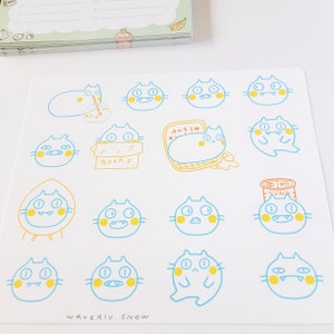 May include: A sheet of stickers featuring 14 different illustrations of blue cats with yellow accents. Each cat has a different expression and is holding or interacting with a different object, such as a book, a can of tuna, or a laptop. The text "WAVERLY SNOW" is printed at the bottom of the sheet.
