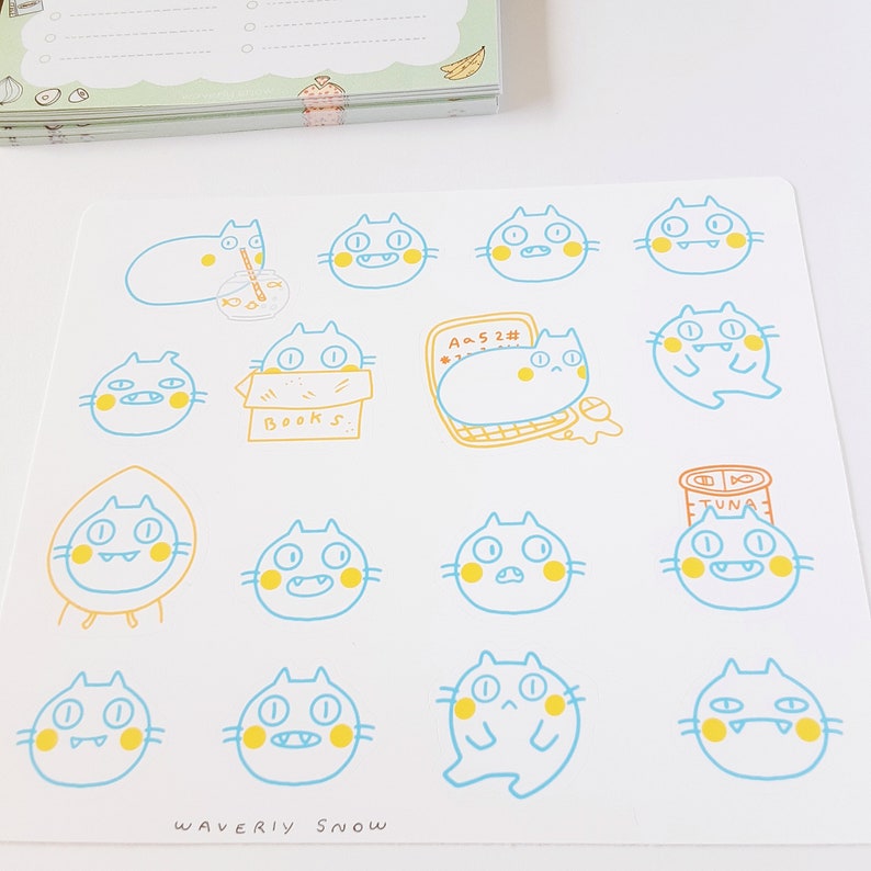 May include: A sheet of stickers featuring 14 different illustrations of blue cats with yellow accents. Each cat has a different expression and is holding or interacting with a different object, such as a book, a can of tuna, or a laptop. The text "WAVERLY SNOW" is printed at the bottom of the sheet.